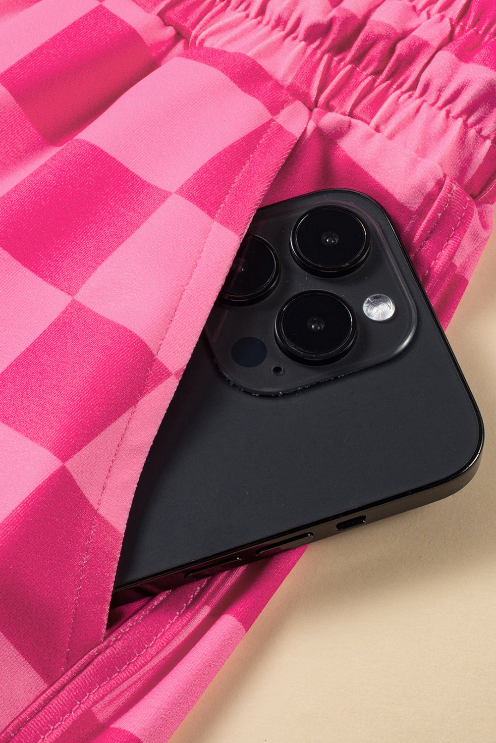 Black smartphone with camera lens on a pink checkered fabric background