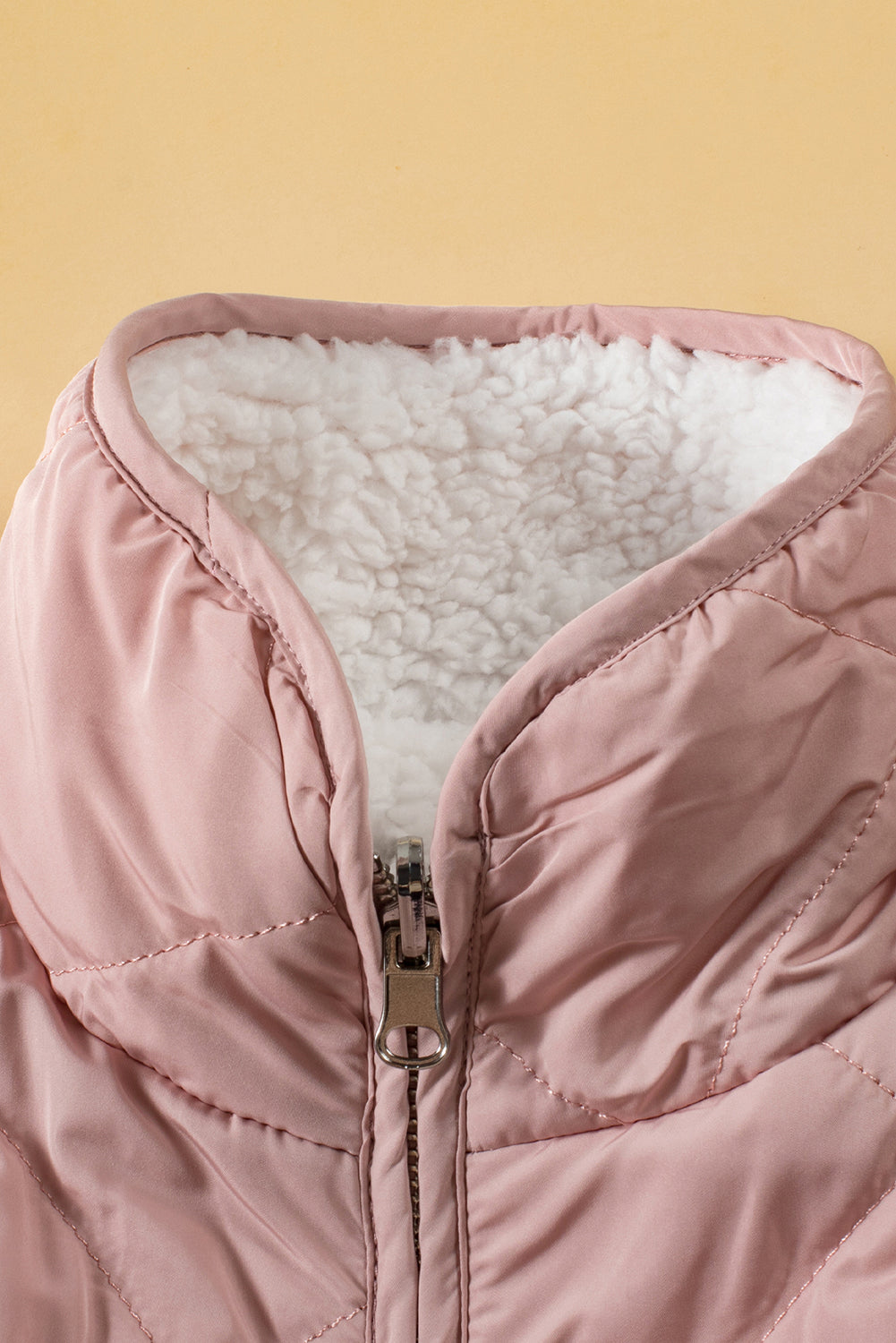 Close-up of a pink quilted jacket with white sherpa lining on a yellow background