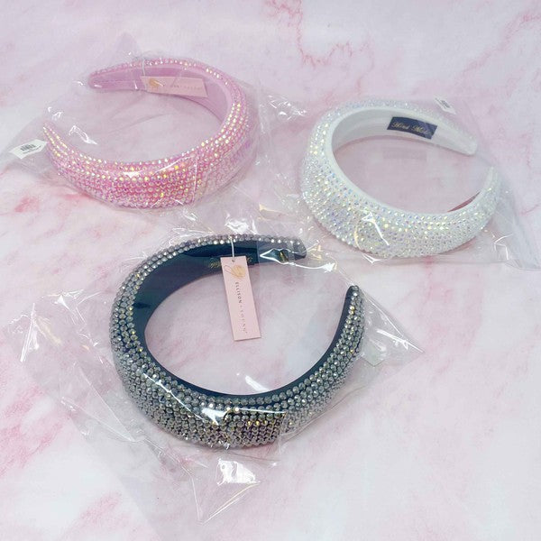 Three rhinestone headbands in pink, black, and white on a pink marble background.