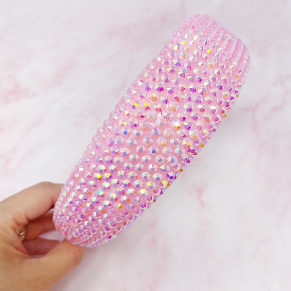 Pink object covered in multicolored rhinestones held by a hand against a pink background