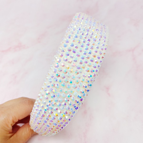 Hand holding a decorative object with colorful bead patterns on a pink background