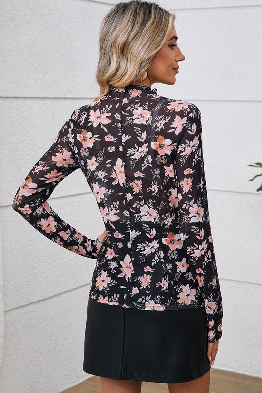 Woman wearing a floral long-sleeve top and black skirt against a light gray wall.