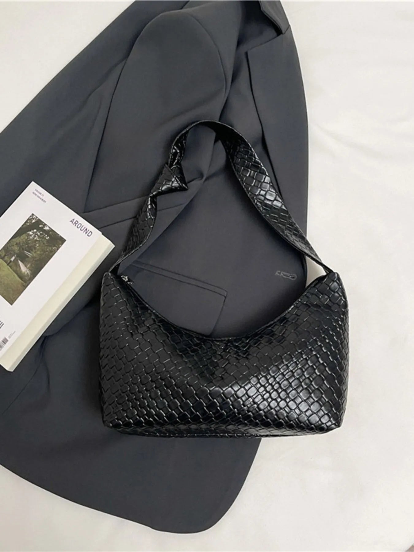 Black textured handbag on a gray surface with a book underneath