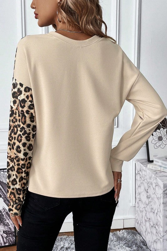 Beige sweater with leopard print sleeves worn by a person indoors.