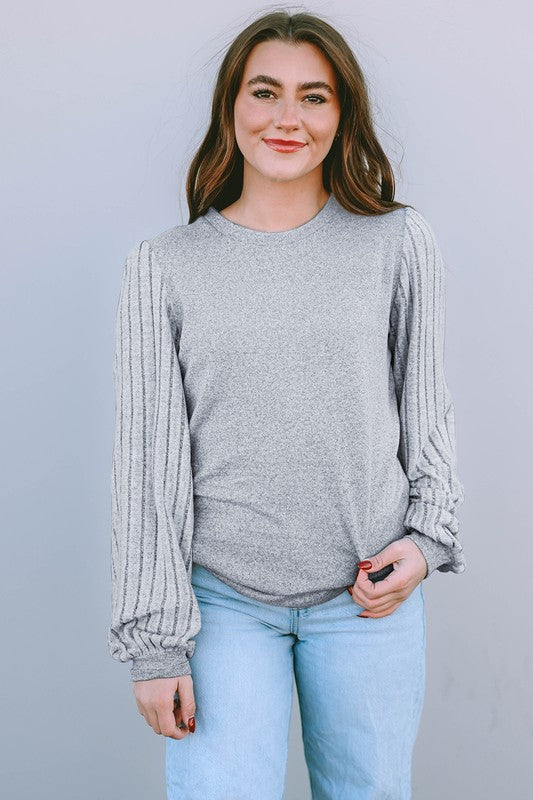 Woman wearing a gray ribbed sweater and light blue jeans against a plain background