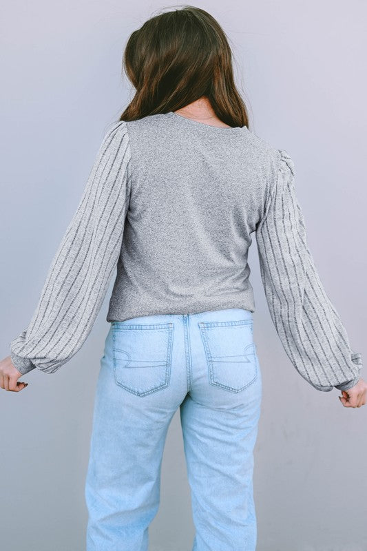 Person wearing a gray long-sleeve shirt and light blue jeans against a plain background