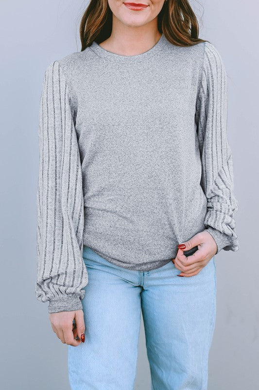 Person wearing a gray ribbed sweater and light blue jeans against a plain background