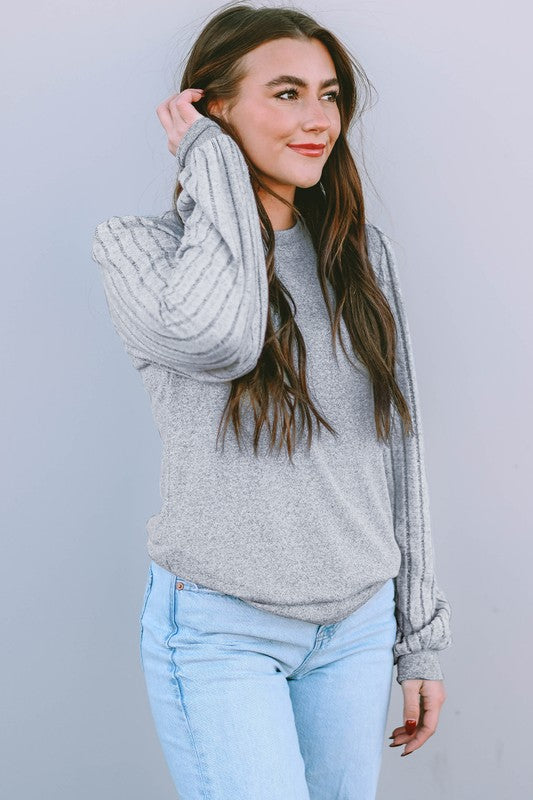 Woman wearing a gray sweater and light blue jeans against a plain background