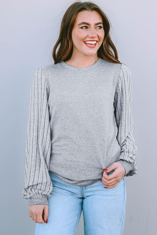 Woman wearing a gray sweater and light blue jeans against a plain background