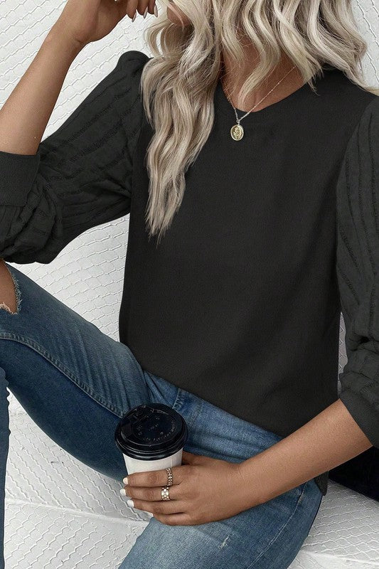 Person wearing a black long-sleeve top and blue jeans, holding a coffee cup.