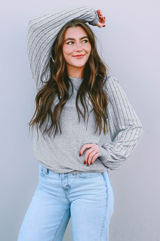 Woman wearing a gray sweater and light blue jeans against a plain background
