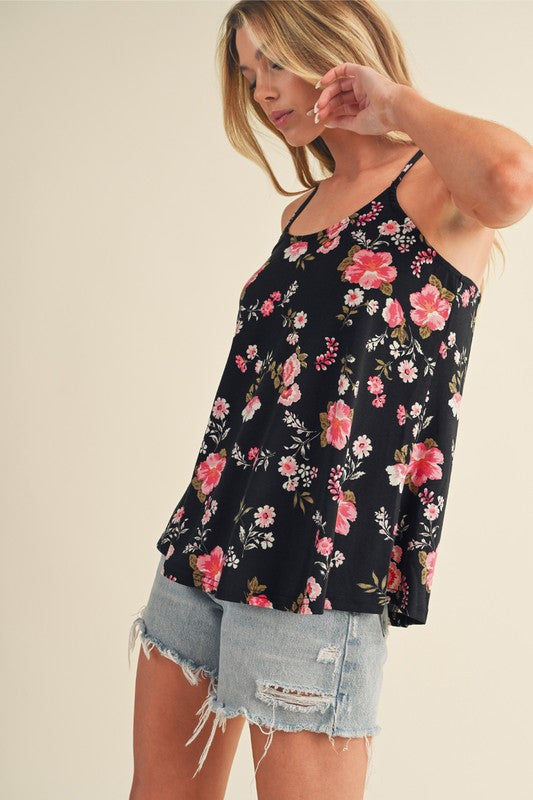 Woman wearing a black floral tank top and denim shorts on a plain background