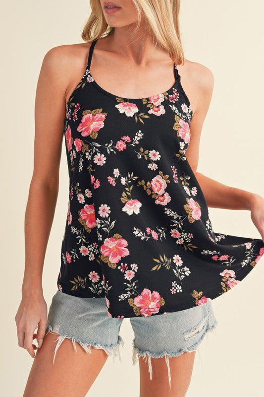 Woman wearing a black floral tank top and denim shorts on a beige background
