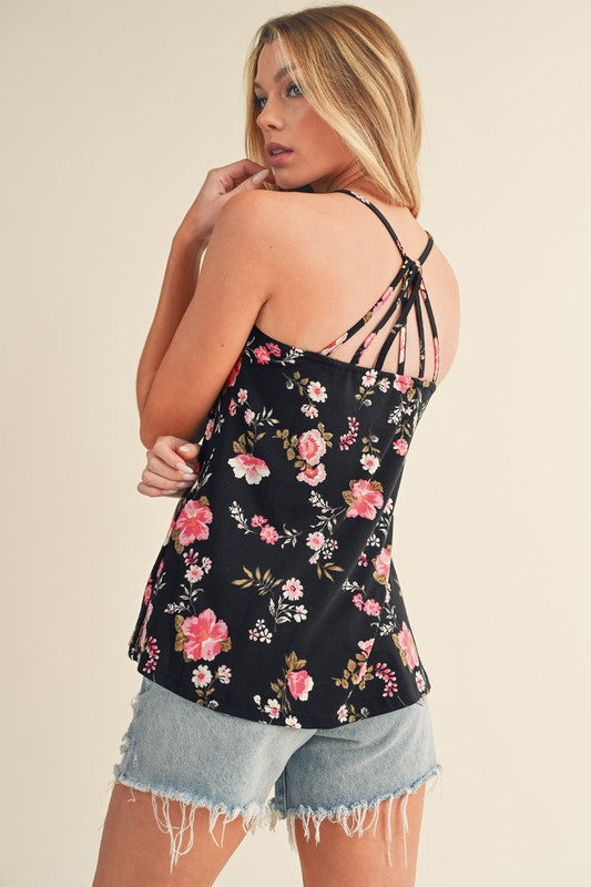Woman wearing a black floral camisole and denim shorts on a beige background