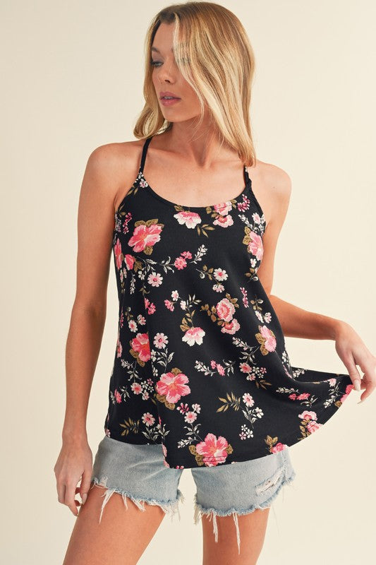 Woman wearing a black floral tank top and denim shorts on a beige background
