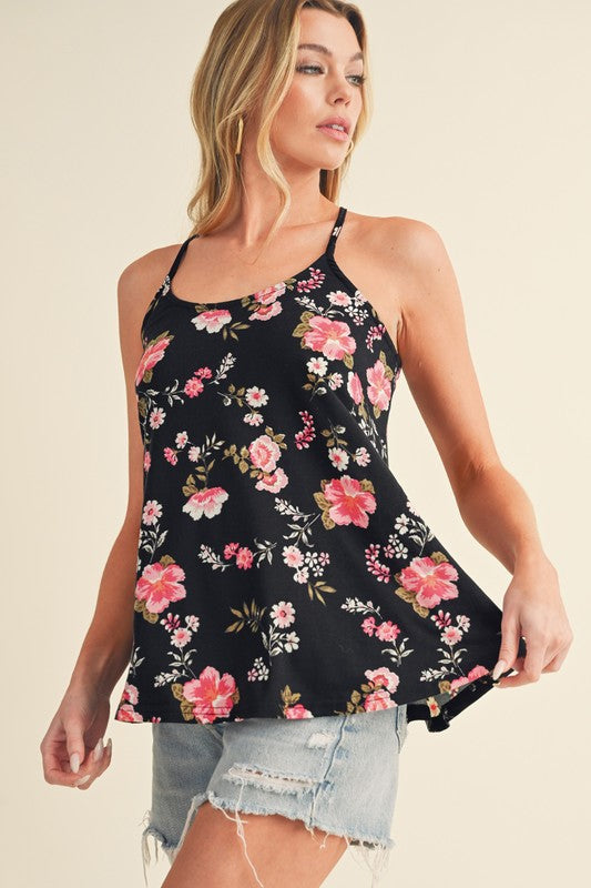 Woman wearing a black floral sleeveless top with denim shorts on a beige background