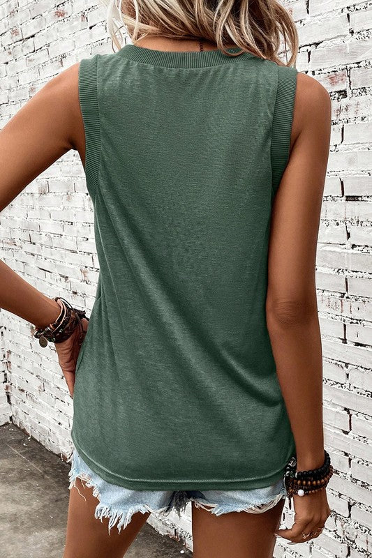 Person wearing a green sleeveless top and denim shorts against a brick wall.
