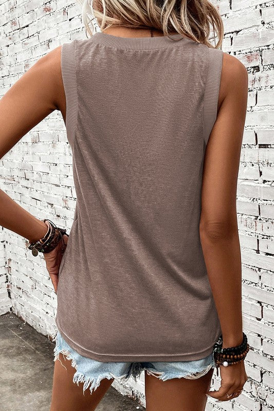 Person wearing a sleeveless brown top and denim shorts against a white brick wall.