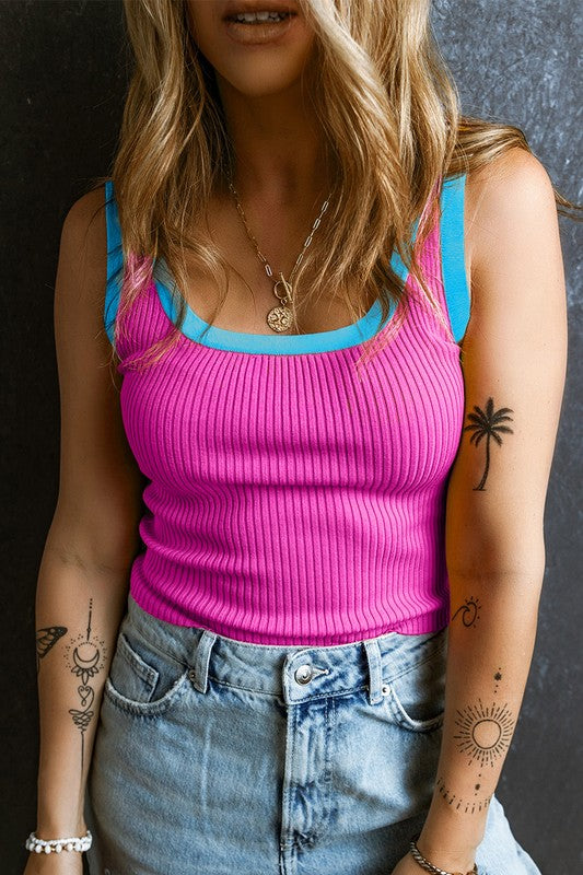 Person wearing a pink ribbed tank top with blue trim and denim shorts against a dark background