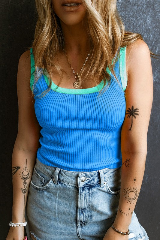 Person wearing a blue tank top and denim shorts with tattoos on arms and neck.