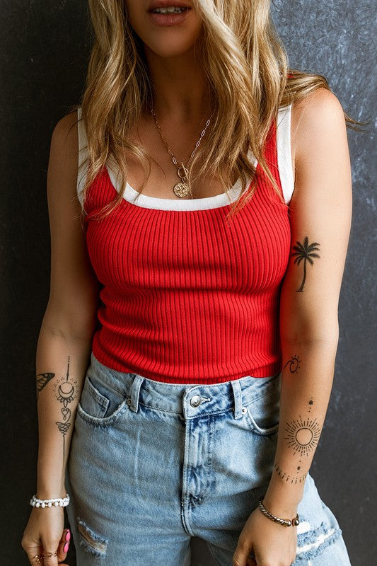 Person wearing a red tank top and blue jeans with tattoos on arms against a dark background