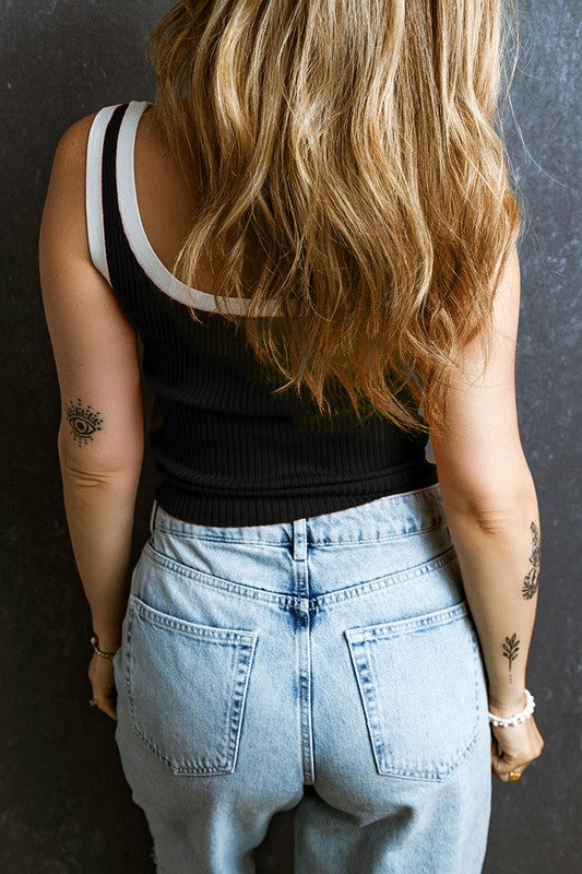 Person wearing a black tank top and light blue jeans with a dark background