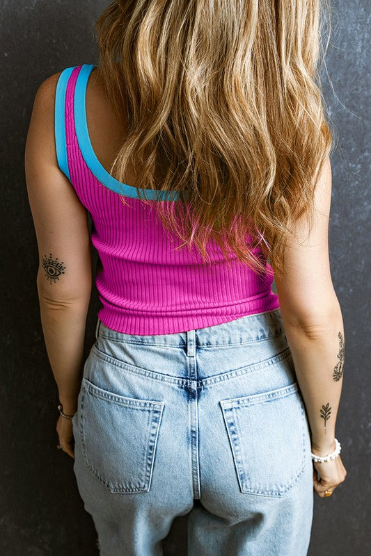 Person wearing a pink tank top with blue straps and light blue jeans against a dark background
