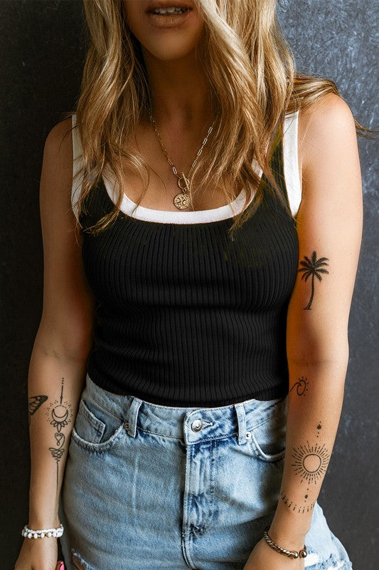 Person wearing a black tank top and blue jeans with tattoos on arms and hands.
