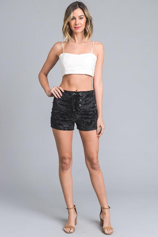 Woman wearing a white crop top and black patterned shorts on a gray background