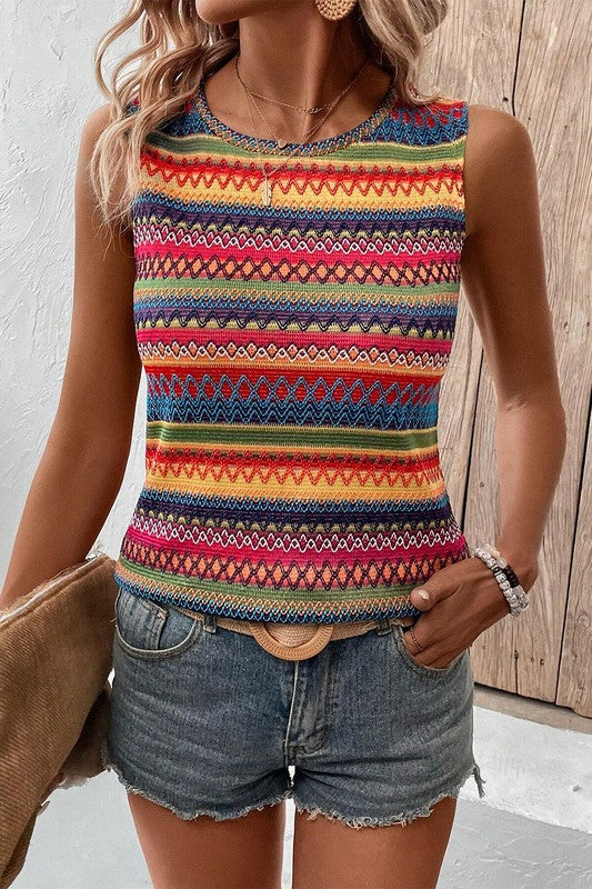 Woman wearing a colorful striped tank top with denim shorts against a wooden wall.