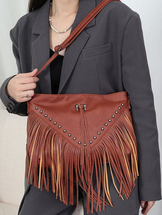 Person holding a brown leather handbag with fringe details against a neutral background