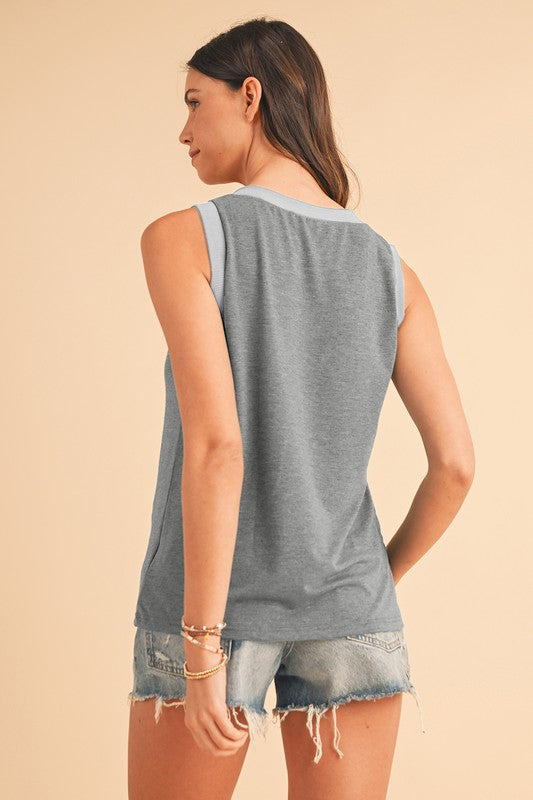 Woman wearing a sleeveless gray top and denim shorts on a beige background