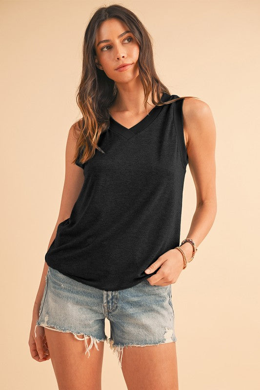 Woman wearing a black sleeveless top and denim shorts on a beige background