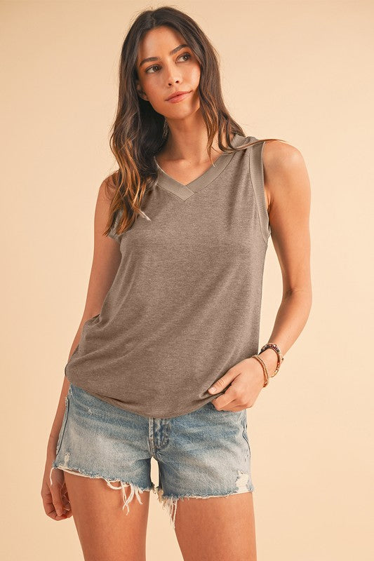 Woman wearing a gray sleeveless top and denim shorts on a beige background