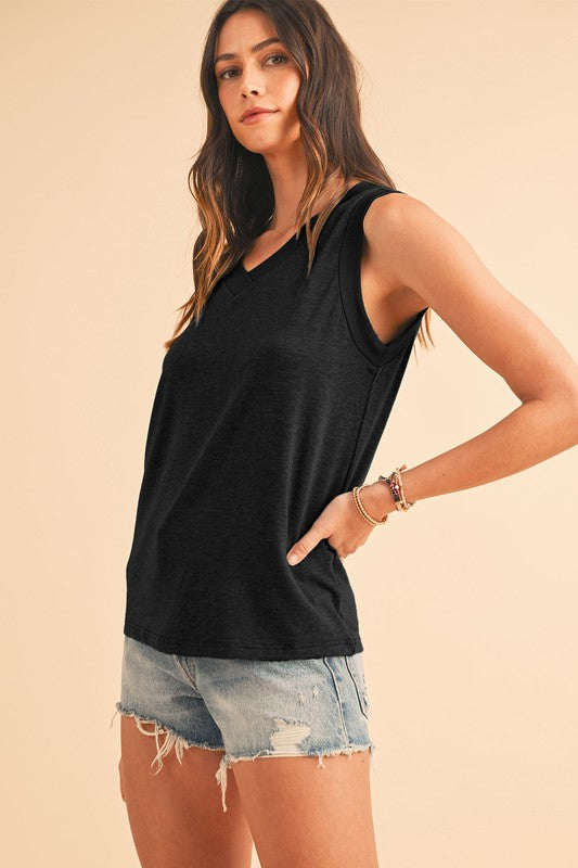 Woman wearing a black sleeveless top and denim shorts on a beige background
