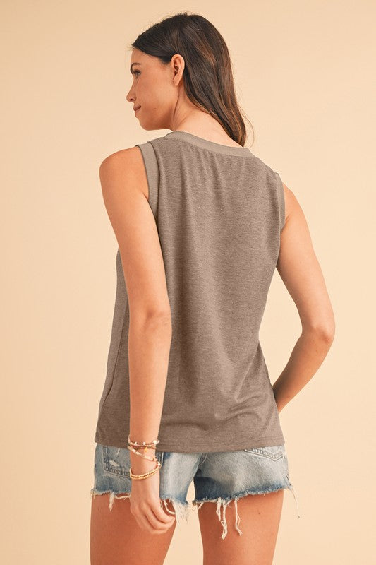 Woman wearing a sleeveless brown top and denim shorts on a beige background