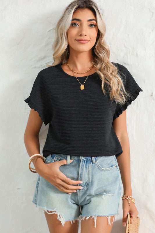 Woman wearing a black top and denim shorts against a white wall