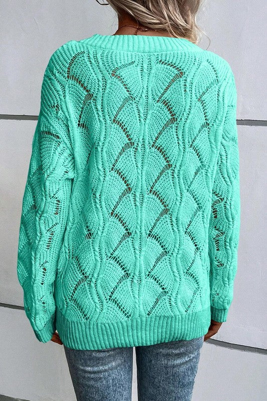 Person wearing a green off-shoulder sweater and blue jeans, holding a coffee cup.