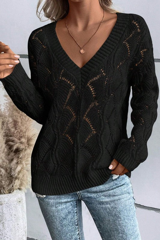 Person wearing a black cable knit sweater with a blurred background