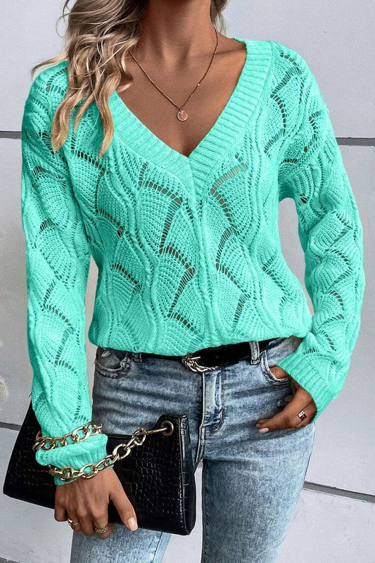 Person wearing a teal knitted sweater and blue jeans with a black clutch.
