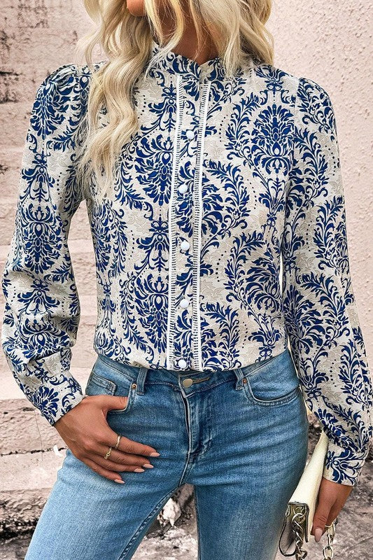 Person wearing a blue and white floral patterned shirt with jeans against a stone wall.