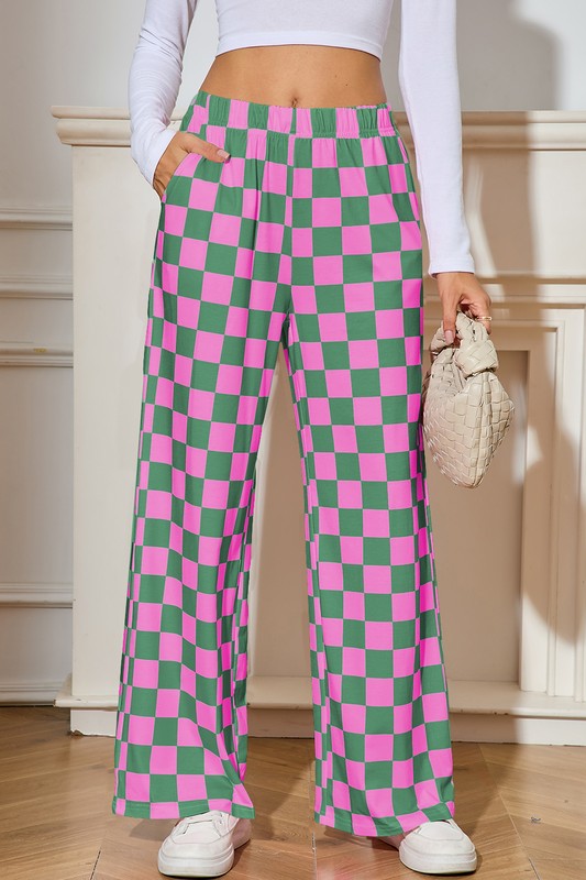 Person wearing pink and green checkered pants with a white top and shoes, holding a beige clutch.