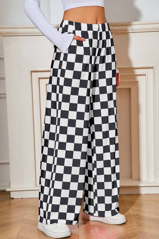Person wearing black and white checkered pants in a room with wooden floor and white walls.