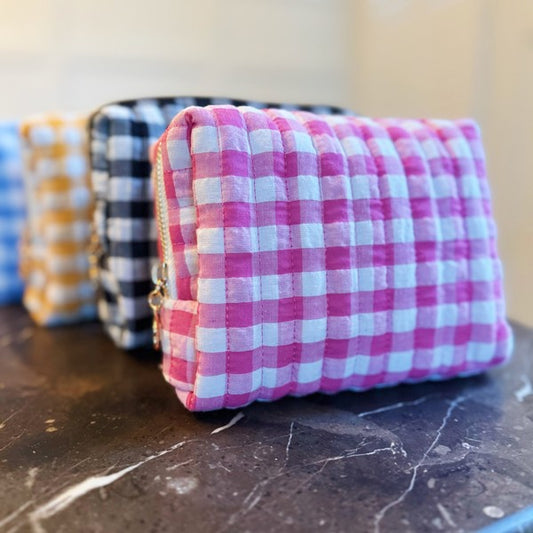 Pink and white checkered pouch on a marble surface with other colorful pouches in the background.