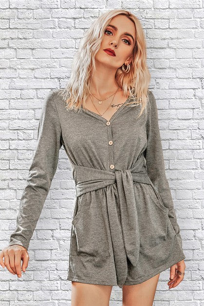 Woman wearing a gray romper against a white brick wall