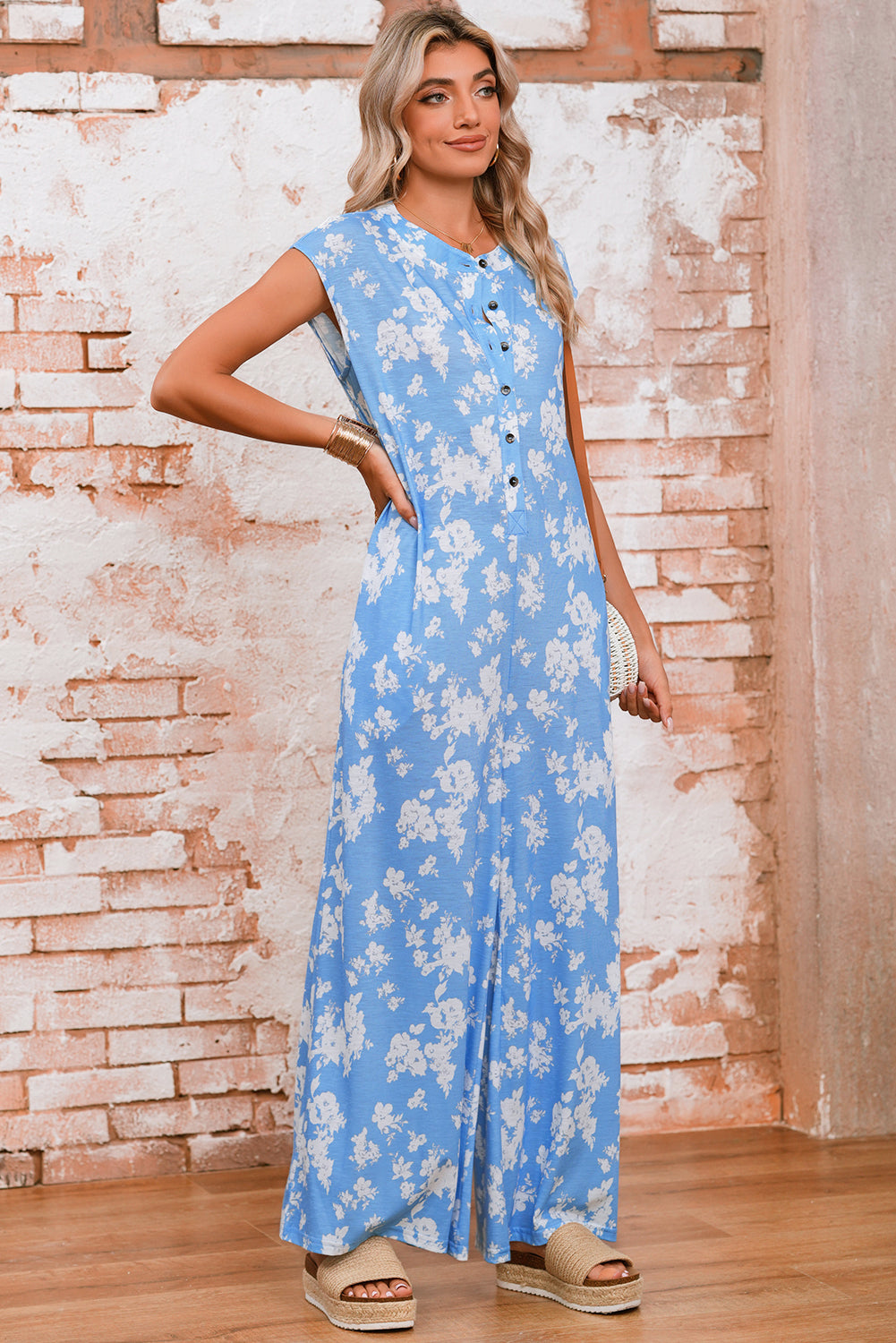 Woman wearing a blue floral dress standing against a brick wall.