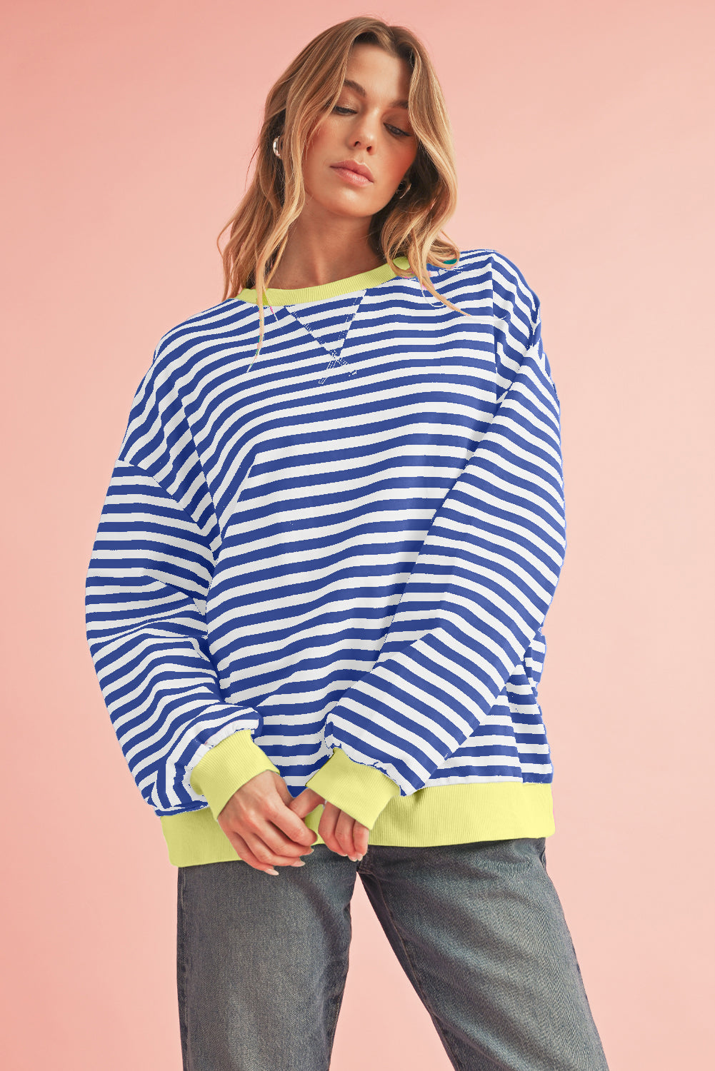 Woman wearing a blue and white striped sweater with green trim on a pink background
