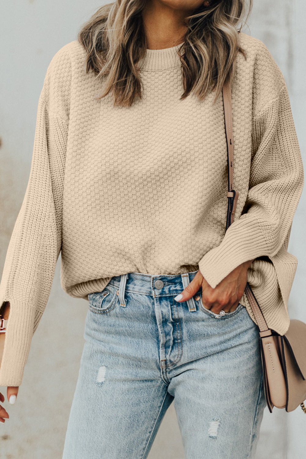 Person wearing a beige sweater and light blue jeans with a neutral background