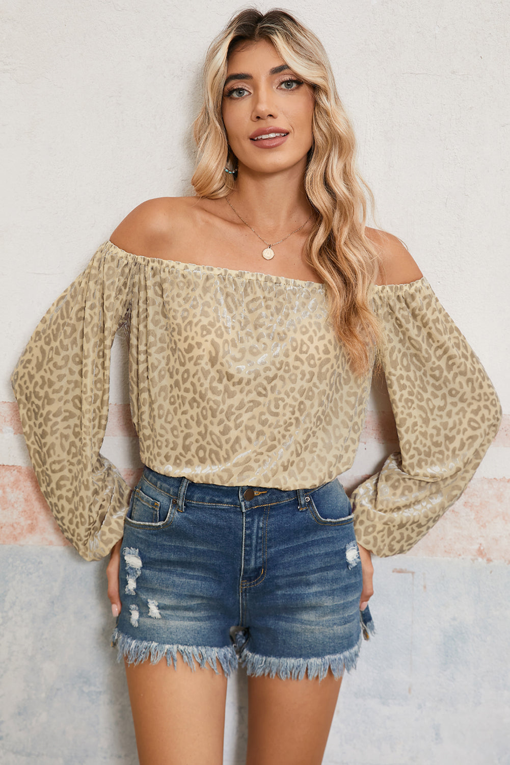 Woman wearing a leopard print off-shoulder top and denim shorts against a light background