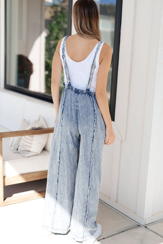 Woman wearing a denim jumpsuit with a white top, standing in an outdoor setting.
